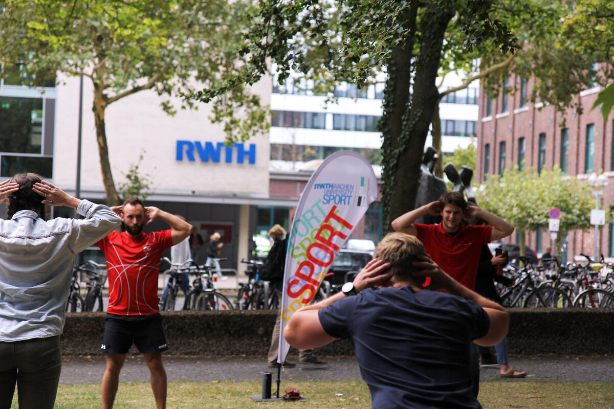 Gruppe von Trainierenden im Park hält die Hände hinter dem Kopf