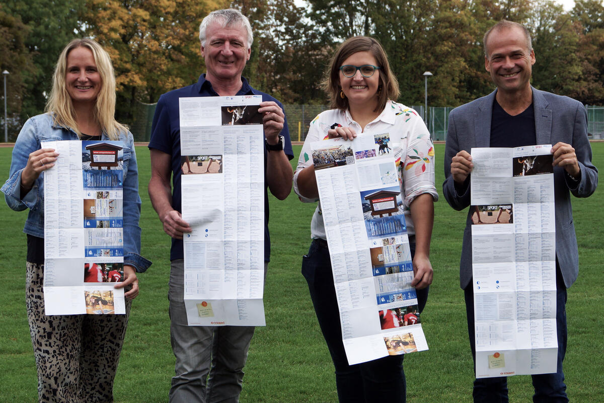 Zwei Frauen  und zwei Männer halten ein Faltblatt vor einem Sportplatz