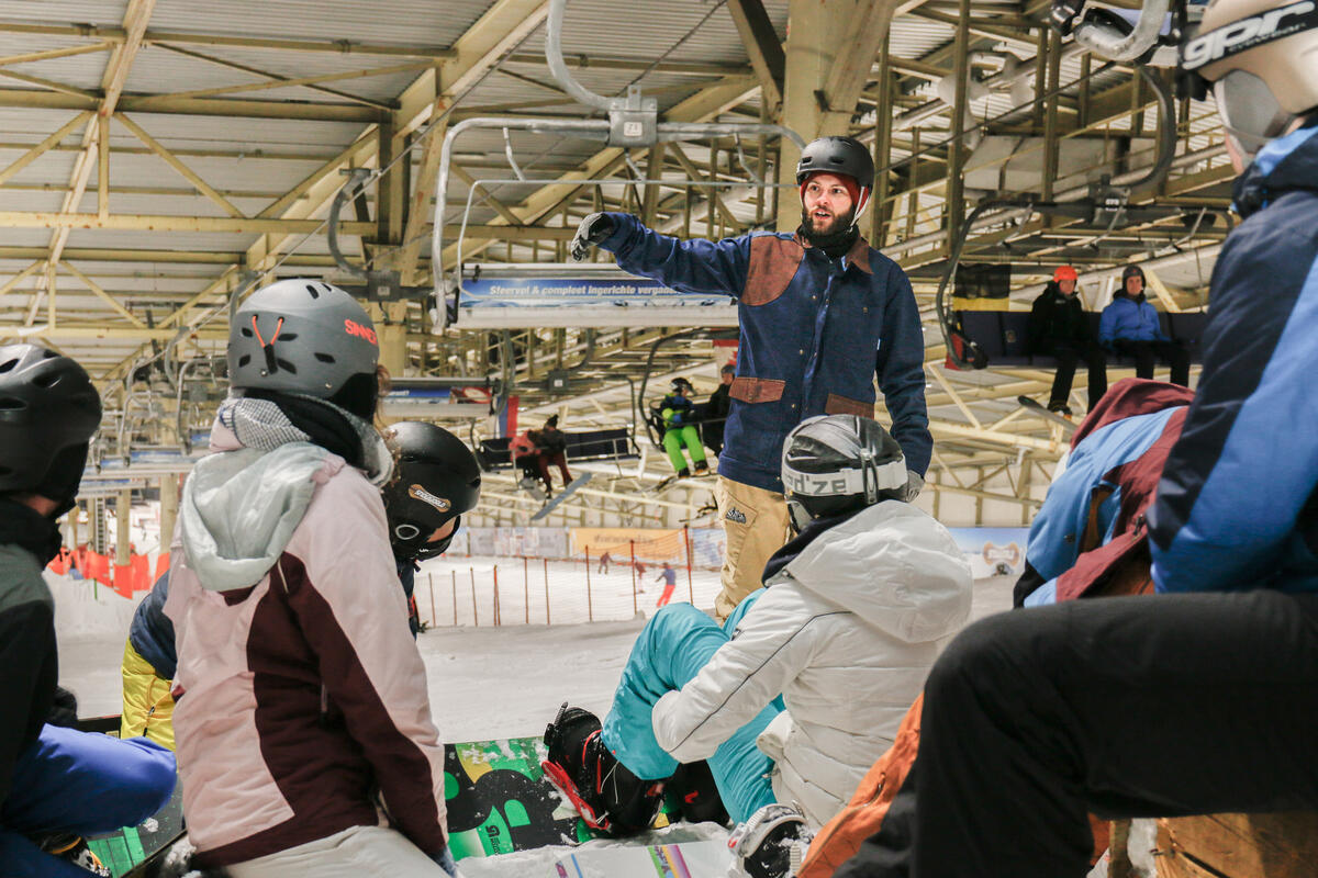 Skilehrer erklärt mit Gesten Snowboard Schülern etwas