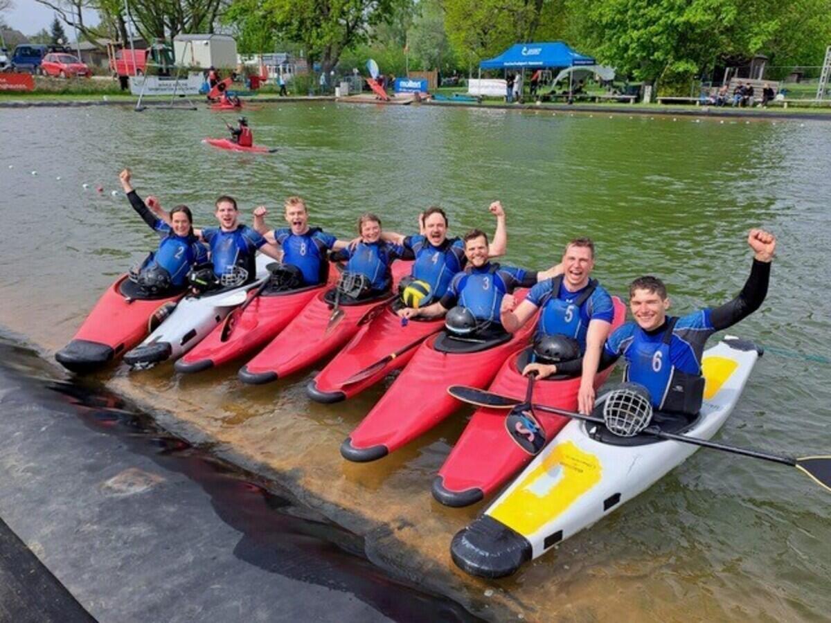 Acht Kanuten sitzen im Kanu auf einem Steg