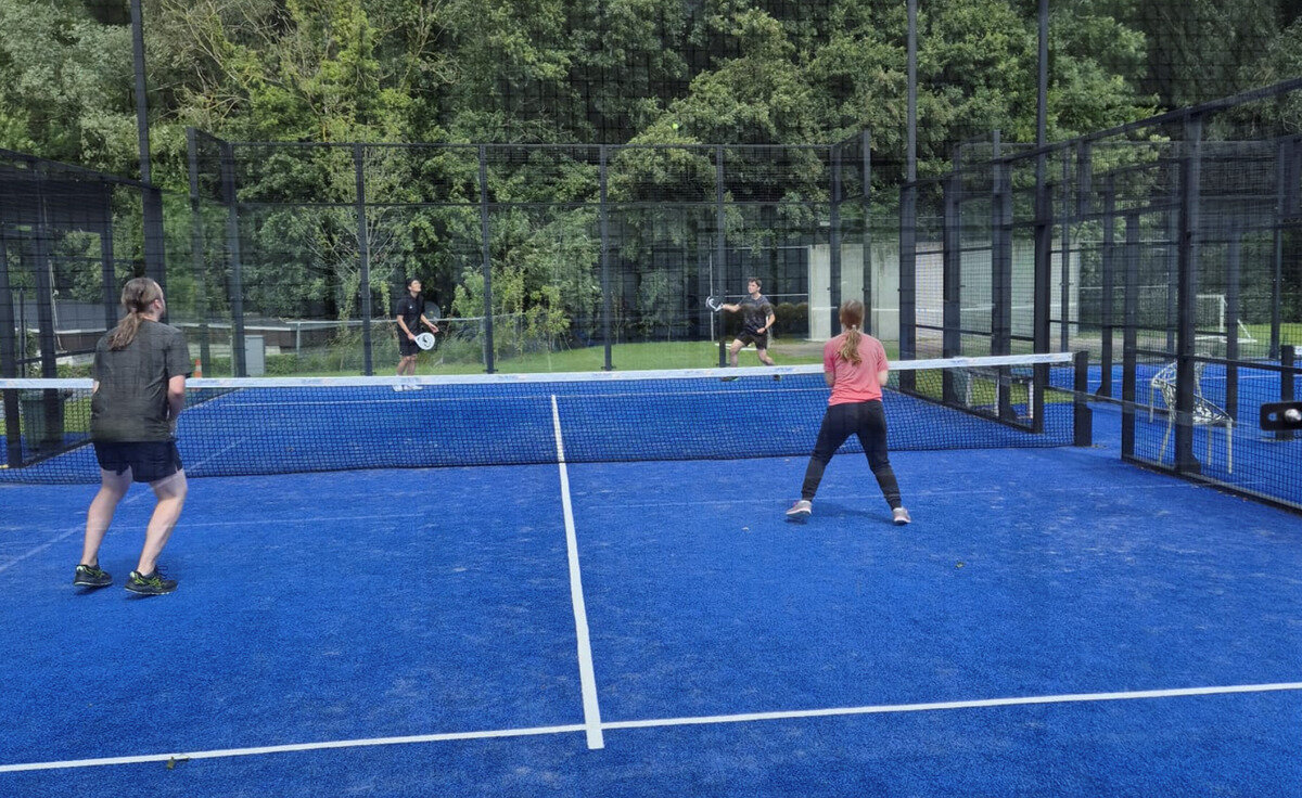 vier Personen spielen Padel auf einem Platz mit einem Netz